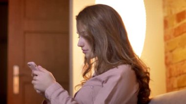 Akıllı telefona dikkatle izlerken ve rahat ev atmosferinde saçlarını ayarlayarak genç kız profili portre.