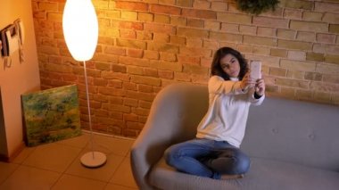 Çekici esmer iş kadını kanepeye oturan ve ev akıllı telefonda selfie-fotoğraf yapma.