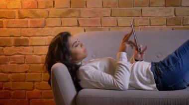 Çekici esmer işkadını kanepede rahatlatıcı ve evde tablet içine izlerken profilinde yakın çekim portre.