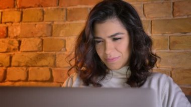 Sevimli beyaz esmer işkadını kanepede oturan ve evde laptop içine gülümseyerek izlerken tam yüzünde portre.