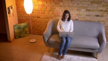 Üst çekim konsantre beyaz brunettehousewife kanepede oturan ve evde dizüstü bilgisayar ile çalışma.