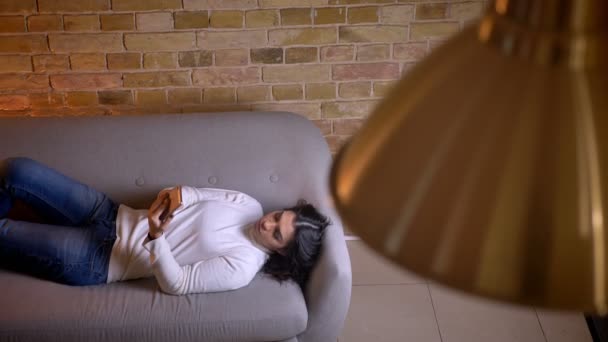 Mulher de negócios morena atraente relaxando no sofá e trabalhando com smartphone em casa . — Vídeo de Stock