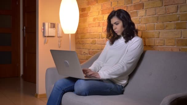 Retrato no perfil de mulher de negócios morena caucasiana atenta sentada no sofá e trabalhando com laptop em casa . — Vídeo de Stock