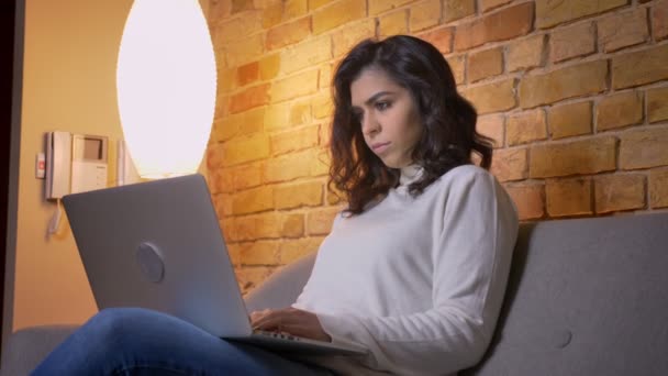 Портрет в профиль концентрированной кавказской брюнетки-предпринимательницы, сидящей на диване и работающей с ноутбуком дома . — стоковое видео