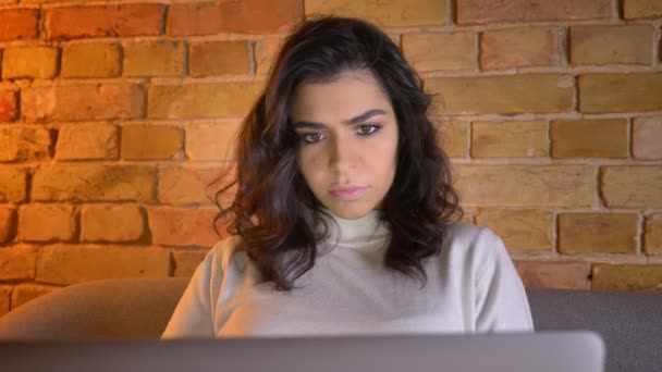 Retrato en plena cara de la atenta mujer de negocios morena caucásica sentada en el sofá y trabajando con el ordenador portátil en casa . — Vídeos de Stock