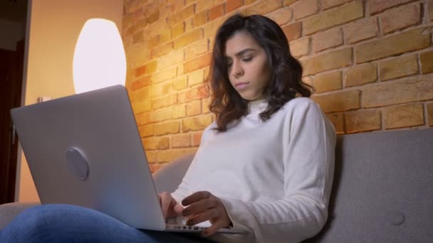 Portrait de profil d'une femme d'affaires brune caucasienne sérieuse assise sur un canapé et travaillant attentivement avec un ordinateur portable à la maison . — Video