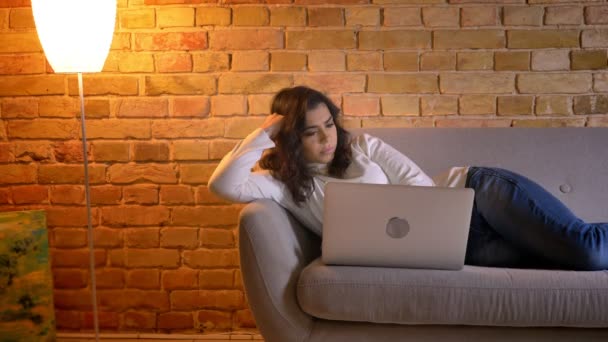 Portré vonzó barna háziasszony pihen a kanapén, és figyeli a laptop otthon. — Stock videók