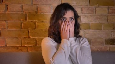Korkmuş beyaz esmer kadın korku filmi izlerken ve rahat ev atmosferinde korku yüzünü kapsayan.
