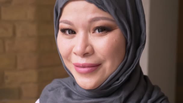 Gros plan sur une employée musulmane adulte en hijab regardant la caméra et souriant joyeusement à l'intérieur sur le lieu de travail — Video