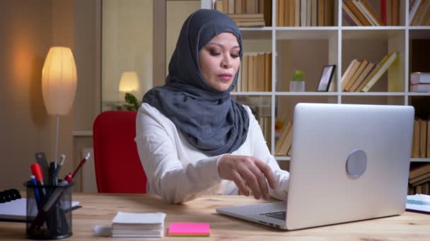 Sesión de cerca de musulmana adulta ocupada mujer de negocios en hijab trabajando en la computadora portátil en el lugar de trabajo en interiores — Vídeos de Stock