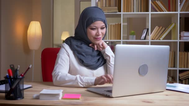 Primo piano ripresa di adulto musulmano dipendente femminile di successo digitando sul computer portatile guardando la fotocamera e sorridendo felicemente sul posto di lavoro al chiuso — Video Stock