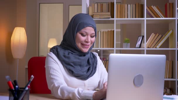 Zbliżenie strzelać dorosłego muzułmańskiego bizneswoman wpisując na laptopie i uśmiechając się wesel na miejscu pracy w pomieszczeniu — Wideo stockowe