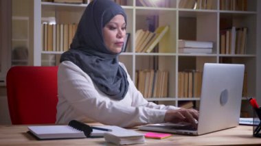 Dizüstü bilgisayar üzerinde hijab yazarak yetişkin Müslüman işkadını ve işyerinde kapalı notlar alarak çekim yan görünüm çekimi