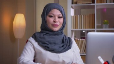 Yetişkin Müslüman işkadını kamera bakıyor ve iş yerinde kapalı neşeli gülümseyen closeup çekim