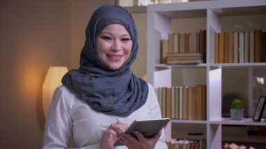 Kamera bakarak tablet kullanarak hijab yetişkin Müslüman kadın çalışanın çekim çekim ve işyerinde kapalı mutlu gülümseyen