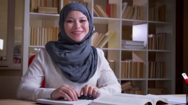 Bir tıbbi sınav için okuyan hijab yetişkin Müslüman kadın doktor çekim çekim kamera mutlu kütüphanede kapalı gülümsüyor bakıyor