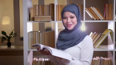 Kamera görünümlü ve kütüphanede kapalı ayakta gülümseyen bir tıbbi sınav için okuyan hijab yetişkin Müslüman kadın doktor closeup ateş