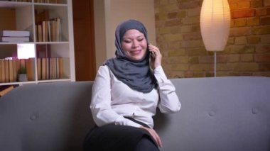 Evde kanepede kapalı otururken bir konuşma telefon ve neşeli gülümsüyor sahip hijab yetişkin Müslüman kadın closeup ateş