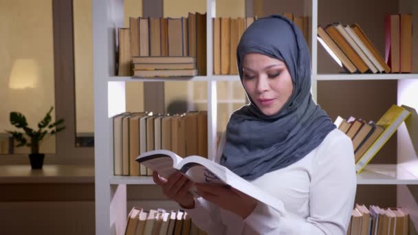 Sesión de primer plano de estudiante musulmana adulta que estudia para un examen médico mirando a la cámara y sonriendo felizmente de pie en la biblioteca en el interior — Vídeos de Stock