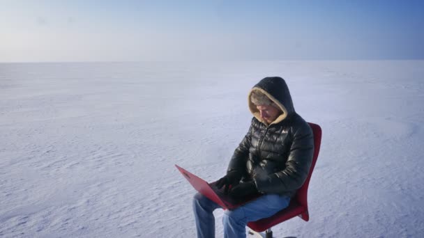 Πορτρέτο του επιχειρηματία σε ζεστό παλτό και κουκούλα κάθεται στο χιόνι έρημο με φορητό υπολογιστή και τεντώνει τον εαυτό του χαρούμενα. — Αρχείο Βίντεο