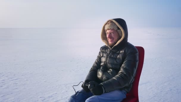 Male player in warm coat and hood wins in videogame and raises his hands in extreme gladness on frozen lake background. — Stock Video