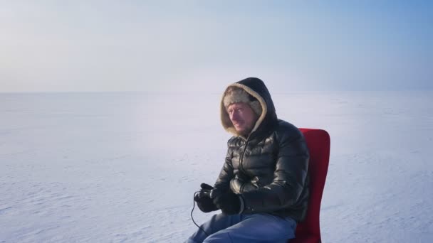 Αθλητής σε ζεστό παλτό και κουκούλα παίζει βιντεοπαιχνίδια και ανεβάζει τα χέρια του σε ευτυχιά μετά τη νίκη σε παγωμένο φόντο λίμνη. — Αρχείο Βίντεο