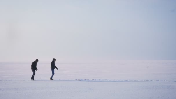 Breed shot van twee mannelijke silhouetten in profiel lopen rechts en een van hen valt en een ander pikt hem uit sneeuw. — Stockvideo