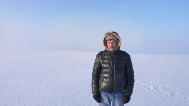 Фотография исследователя средних лет, спокойно и серьезно смотрящего на дистанционную камеру на фоне снежной пустыни . — стоковое видео