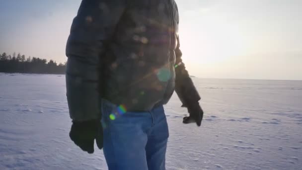Выстрел мужских ног в профиль, идущих вправо под солнцем на снежном поле . — стоковое видео