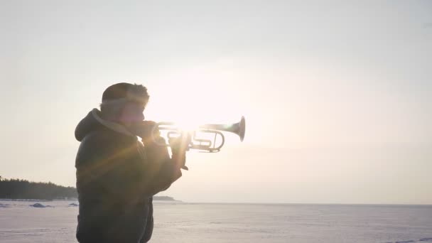 Porträt eines kaukasischen Musikers, der bei Sonnenschein auf gefrorenem Naturhintergrund Trompete spielt. — Stockvideo