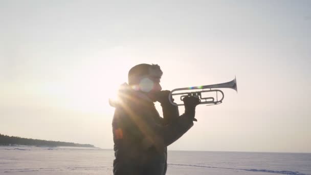 Retrato en perfil de músico caucásico solo tocando trompeta activamente bajo el sol sobre fondo congelado de la naturaleza . — Vídeo de stock