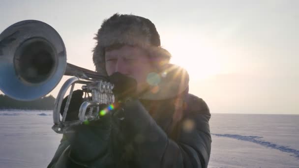 在冰冻的自然背景下, 严重的高加索音乐家在阳光下吹喇叭的特写镜头. — 图库视频影像