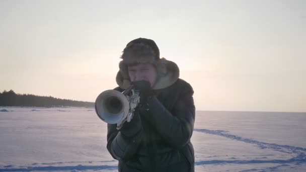 Nahaufnahme Porträt eines ernstzunehmenden kaukasischen Musikers, der aktiv Trompete spielt im Sonnenschein auf winterlichem Naturhintergrund. — Stockvideo