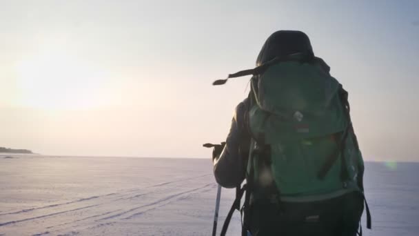 Retrato trasero mochilero masculino con palos de montaña y bolsa enorme caminando por el campo cubierto de nieve . — Vídeos de Stock