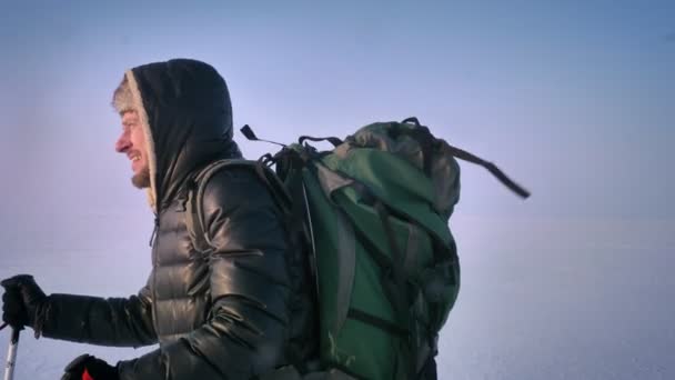 Retrato en perfil de mochilero agotado con palos de montaña y enormes paseos en bolsa con dificultad a lo largo del campo nevado . — Vídeos de Stock