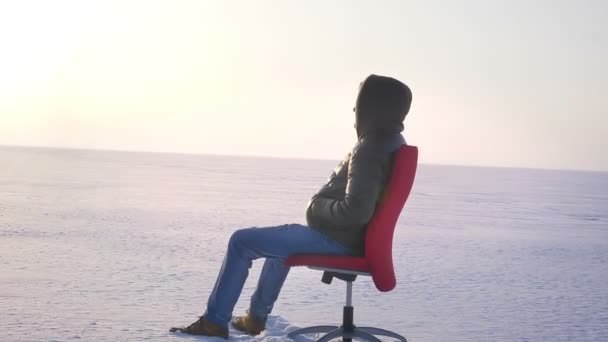 在雪场背景下, 独自的商人坐在红椅上, 望着远处的镜头. — 图库视频影像