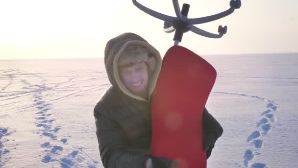 Nahaufnahme eines Sportlers in warmem Mantel und Kapuze, der einen schweren roten Stuhl auf der Schulter auf Schneefeld-Hintergrund trägt. — Stockvideo