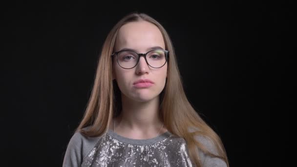 Vértes lő a fiatal, vonzó csípő női szemüveg, hogy zavaros és átgondolt nézett egyenesen a kamera elszigetelt fekete háttérrel — Stock videók