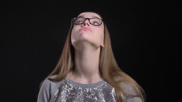 Nahaufnahme einer jungen attraktiven Hipster-Frau mit Brille, die gelangweilt und desinteressiert direkt in die Kamera blickt, mit einem auf schwarz isolierten Hintergrund — Stockvideo