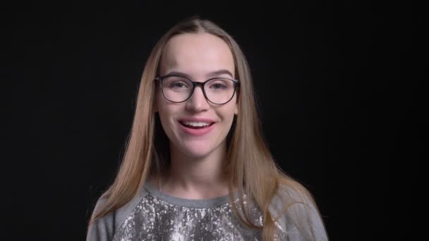 Vértes lő a fiatal, vonzó csípő női szemüveg mutatja a nyelv és a játék egy bolond nézett egyenesen a kamera elszigetelt fekete háttérrel — Stock videók