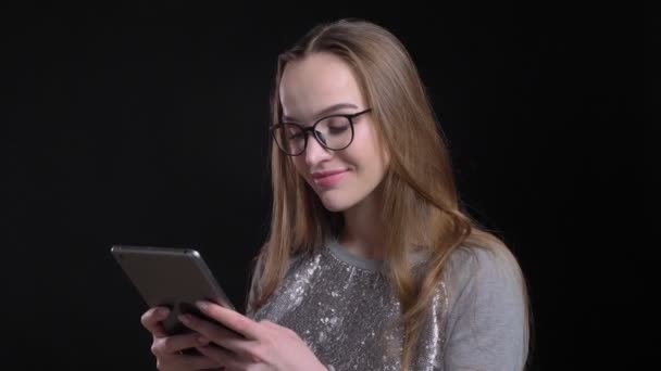 Brote de primer plano de joven atractiva hembra hipster en gafas usando la tableta con fondo aislado en negro — Vídeos de Stock