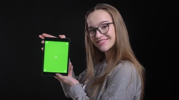 Nahaufnahme einer jungen attraktiven Hipsterfrau in Brille, die das Tablet benutzt und der Kamera den grünen Bildschirm zeigt, mit einem auf schwarz isolierten Hintergrund — Stockvideo