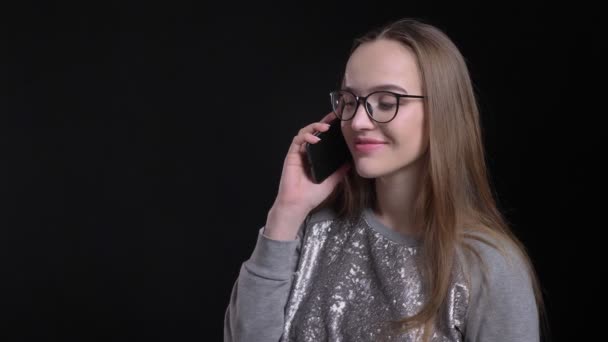 Primer plano de disparar de joven atractivo hipster hembra en gafas tener una conversación por teléfono con fondo aislado en negro — Vídeos de Stock