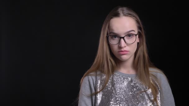 Съемки крупным планом молодой привлекательной хипстерки в очках, разочарованной и расстроенной, смотрящей прямо в камеру с изолированным на черном фоне — стоковое видео