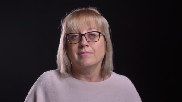 Lähikuva ampua vanhempi valkoihoinen blondi nainen lasit saada innoissaan ja juhlii kameran edessä tausta eristetty musta — kuvapankkivideo