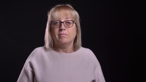 Primer plano de la vieja rubia caucásica en gafas sonriendo alegremente y saludando con el fondo aislado en negro — Vídeos de Stock