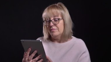 Eski Beyaz sarışın büyükanne ile arka plan üzerine siyah izole kamera önünde tablet socail medya sörf bardaklarda portre çekimleri