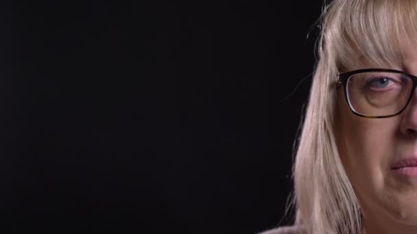 Closeup poloobličejových natáčení starých kavkazské blond ženská tvář v brýlích s pozadím při pohledu přímo na kameru, samostatný na černém pozadí — Stock video