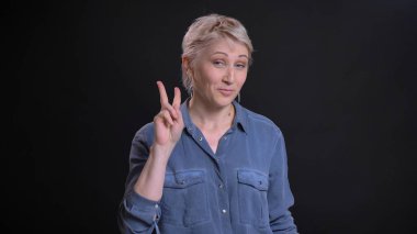 Tatlı bir zafer işaret gösteren ve neşeyle kameraya bakarken gülümseyen yetişkin çekici beyaz kadın portresi