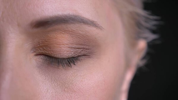 Closeup half-face shoot of young attractive caucasian female with blue eye being closed in front of the camera